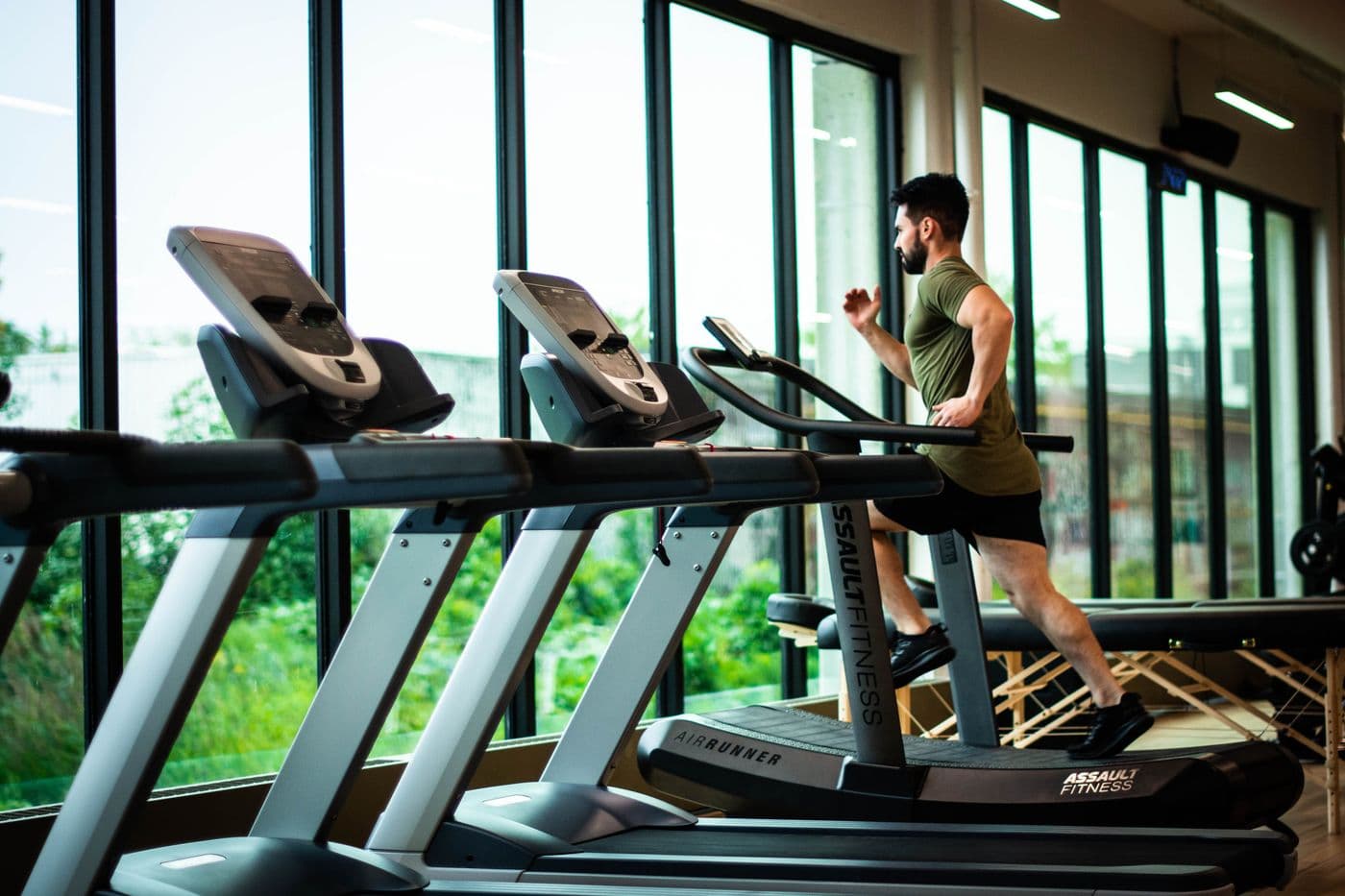 Rangée de tapis de course devant les baies vitrées d'une salle de sport